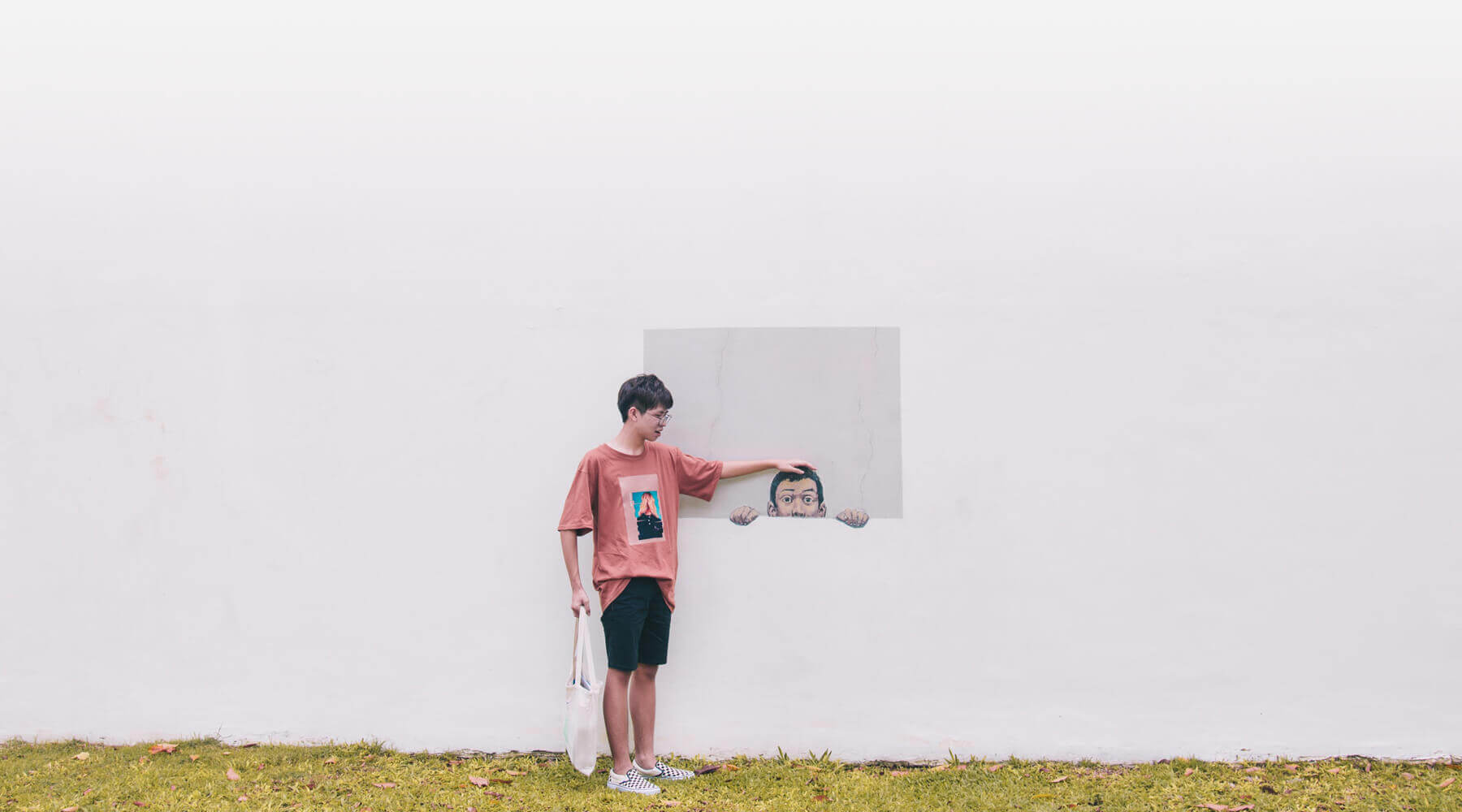 Photo of a boy standing in the grass, in front of a painting on a concrete wall