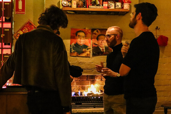 Adam and some members standing around an open fireplace, talking and drinking