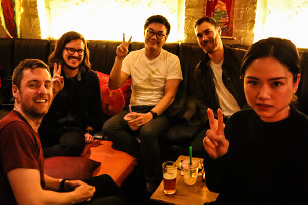 Group of members sitting down and looking at the camera while giving the 'peace' sign