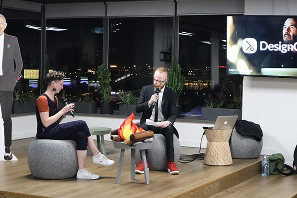 Milly and Adam having a fireside chat on stage, with a video of Keanu Reeves in the background